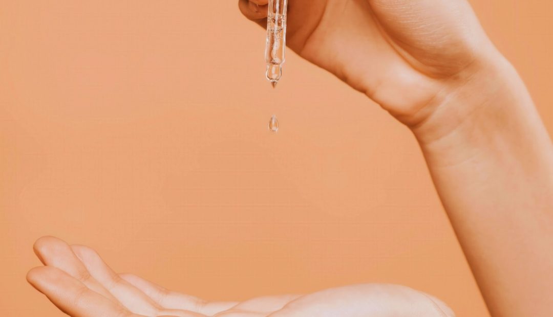 Goutte de sérum de soin qui tombe d'une pipette dans une main
